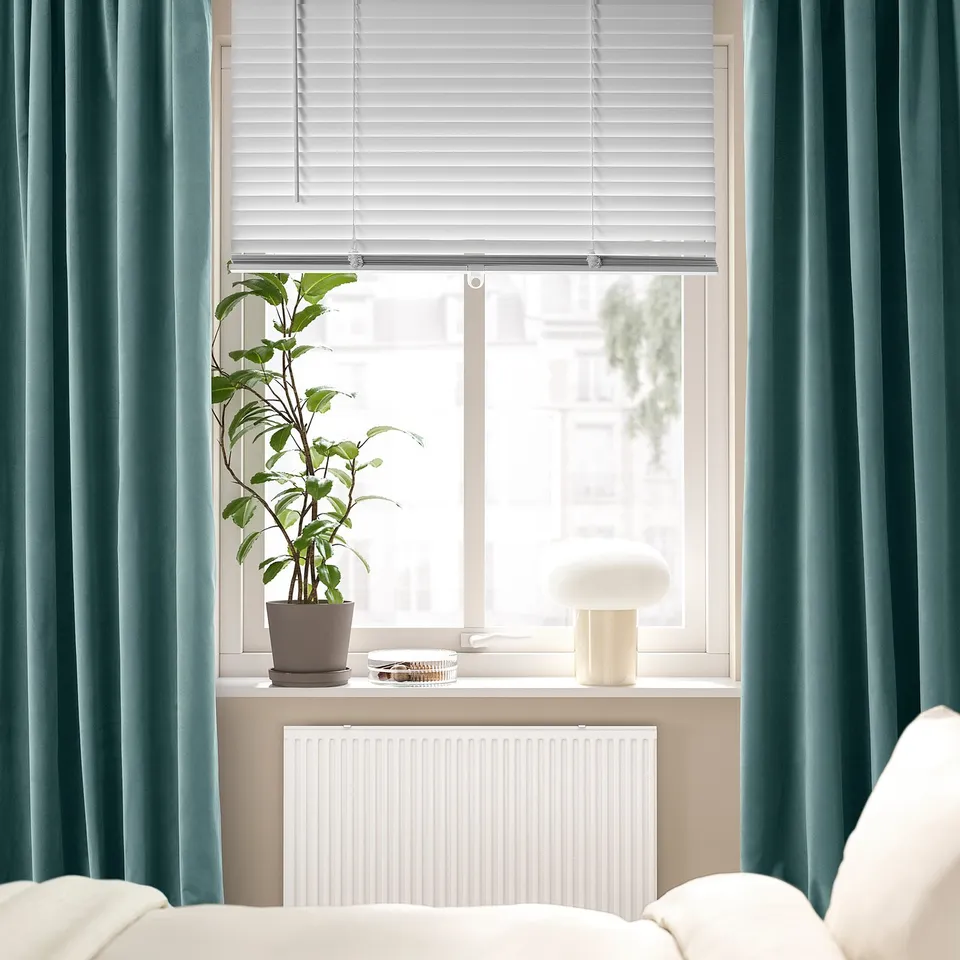 Window with white blinds, plant, lamp, blue curtains, radiator below.