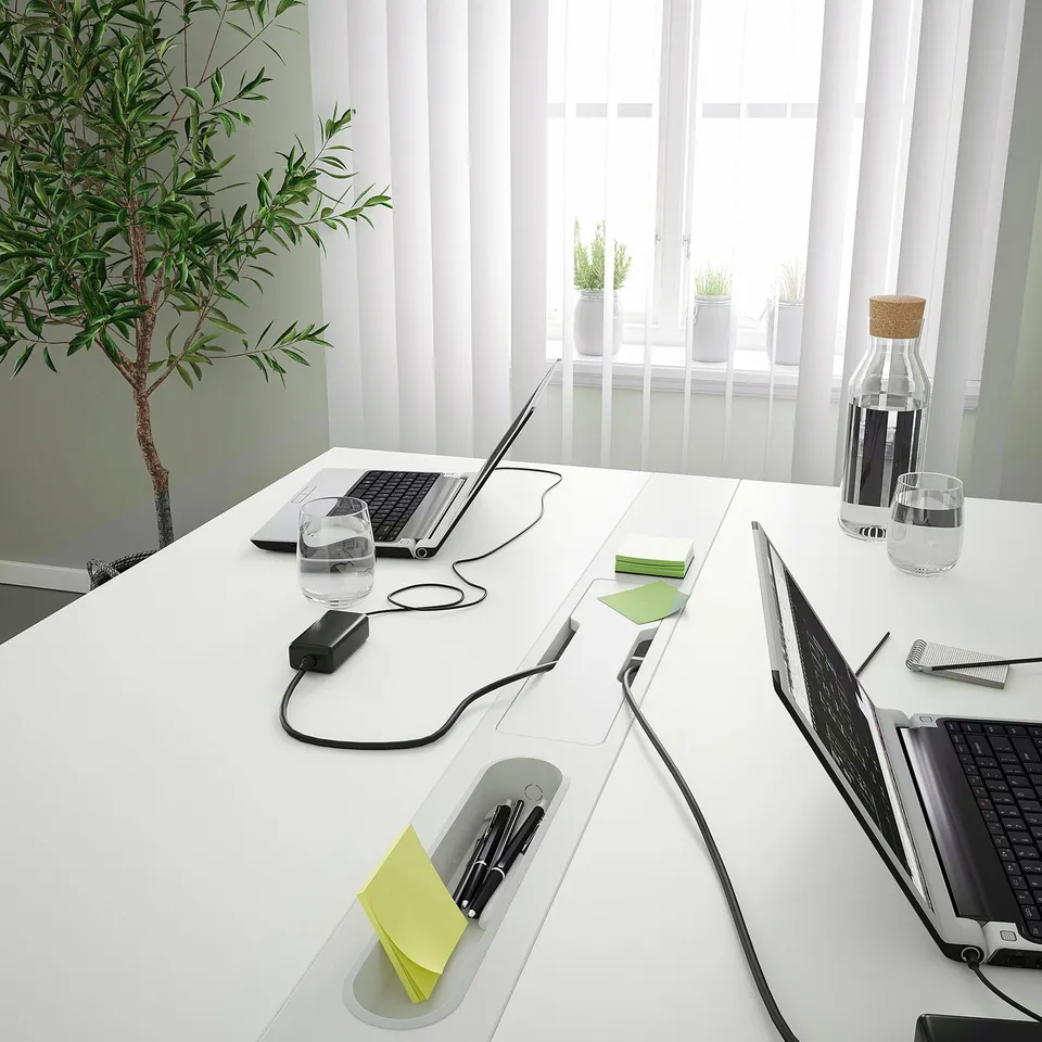 Modern conference table with laptops and notepads, ready for a meeting. Lots of workspace and organised with cable management and water bottles.