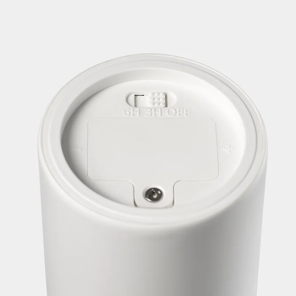 Close-up of white battery-operated led candle top, showing smooth surface, on/off button, and timer symbols.