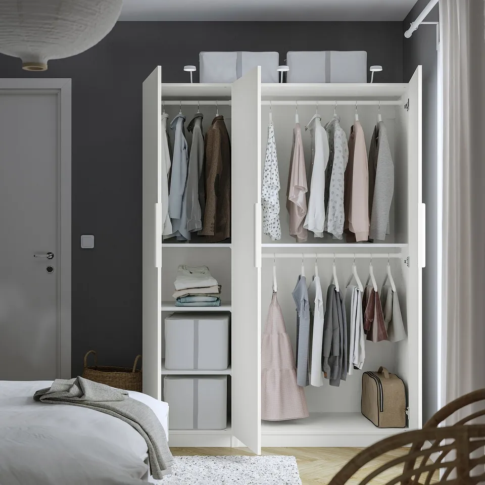 Open wardrobe showing organised clothes, with adjustable shelves and compartments, positioned accanto to bed in a bedroom.