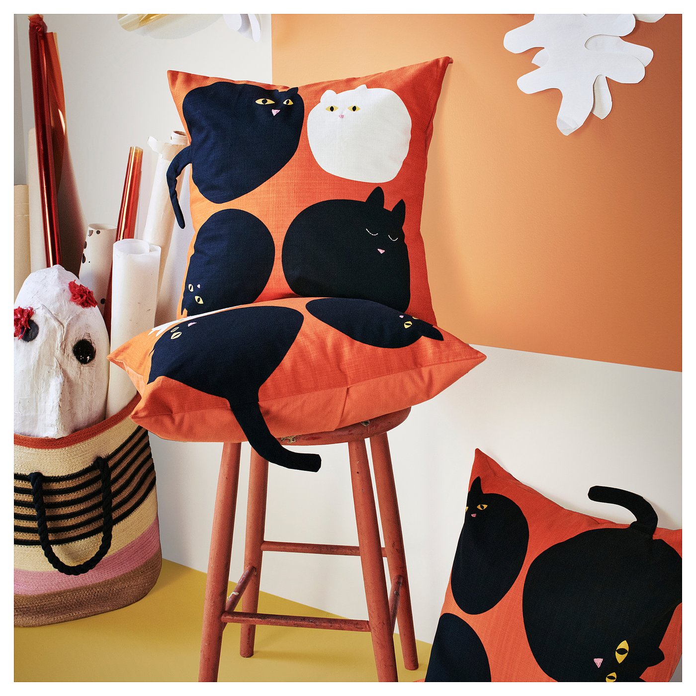 Orange stool with cat-faced cushions, black and white cats on red covers, striped bag, vibrant decor.
