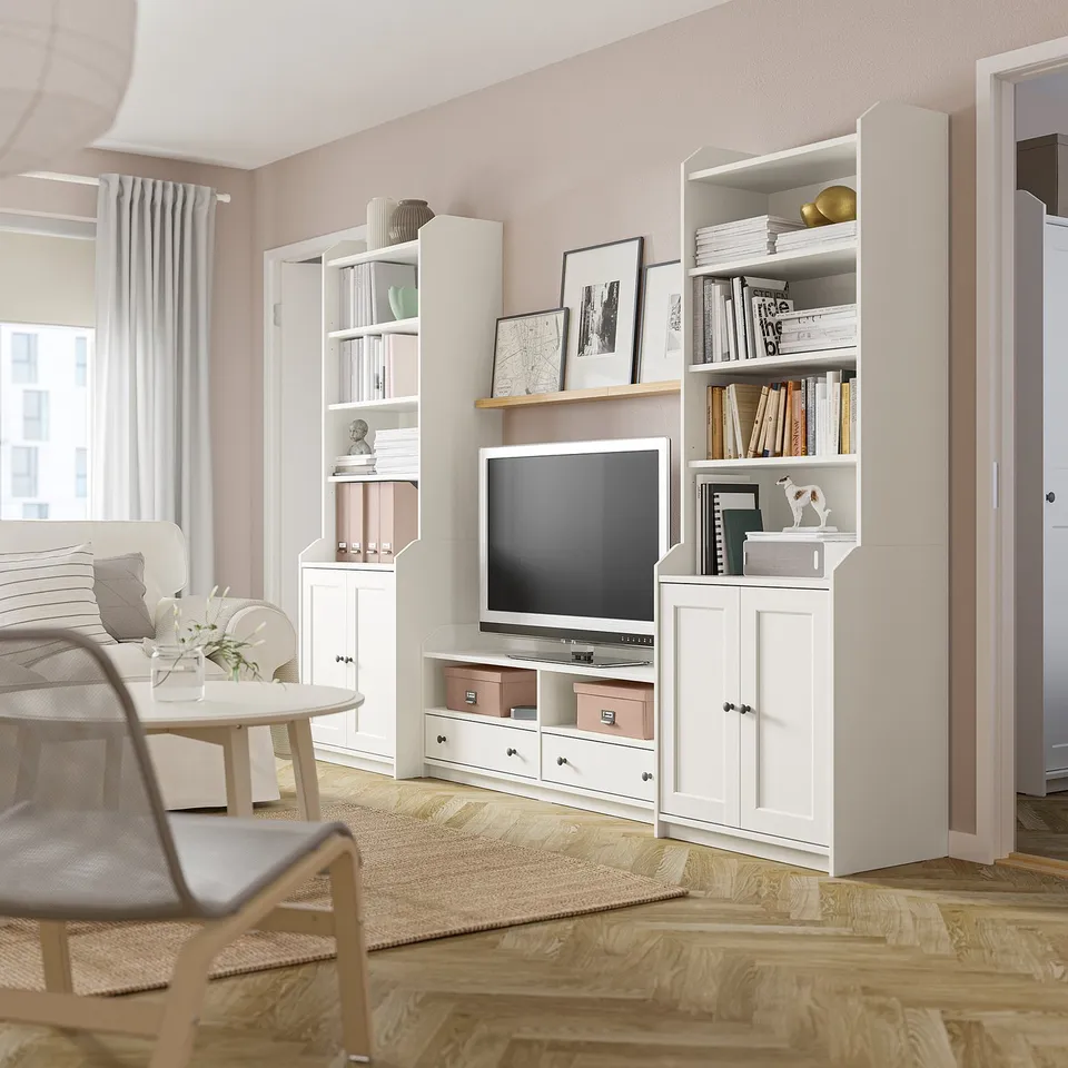 Living room with HAUGA white tv unit and shelves, holding books and decor. Light wood floor, beige rug, and curtains.