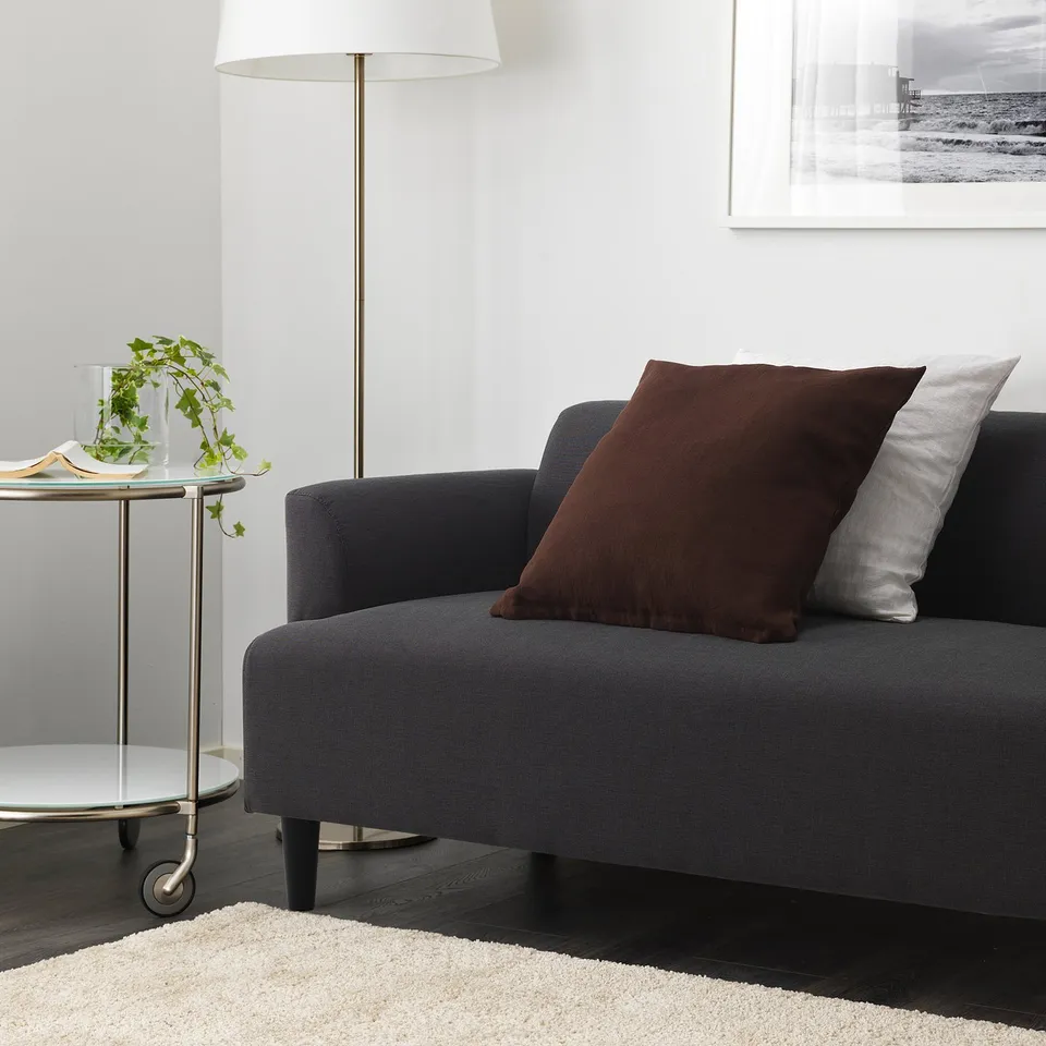 Grey HEMLINGBY sofa with pillows, side table with plant and book, wall lamp and photo.