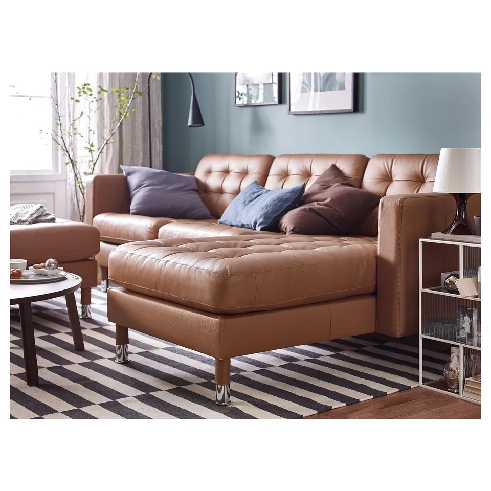Modern living room with a brown leather l-shaped sofa and an ottoman, striped rug, wooden side table, and bookshelf.