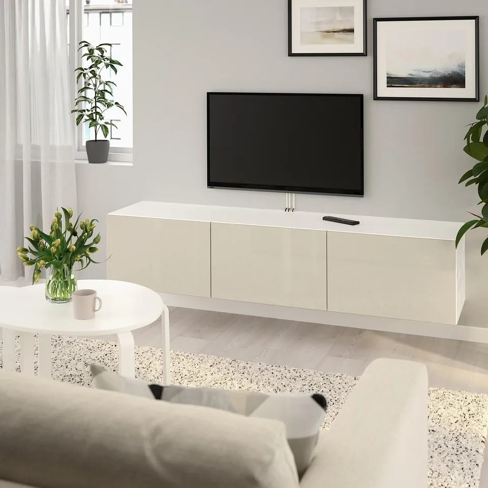 Modern living room with BESTÅ tv bench, plants, art, coffee table, and couch on light wood floor.
