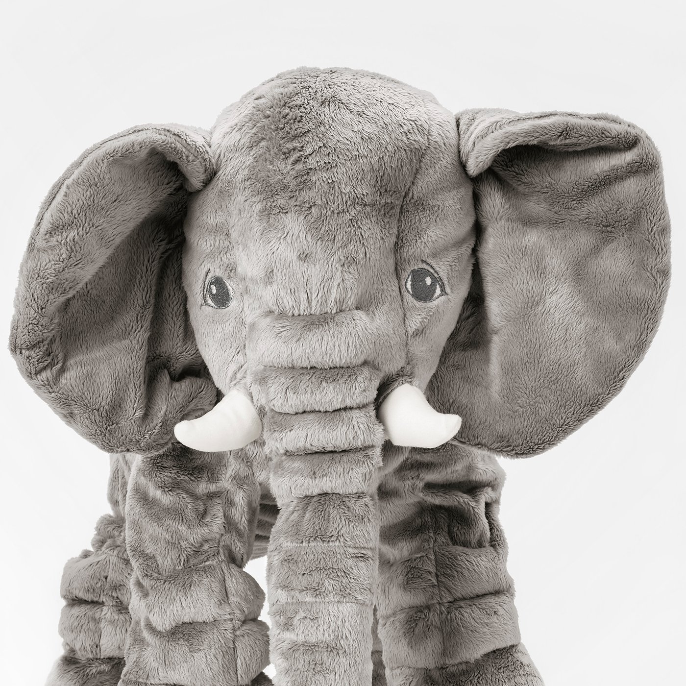 Stuffed elephant toy with large floppy ears and white tusks, made from soft grey fabric. Its trunk is a plush, inviting texture.