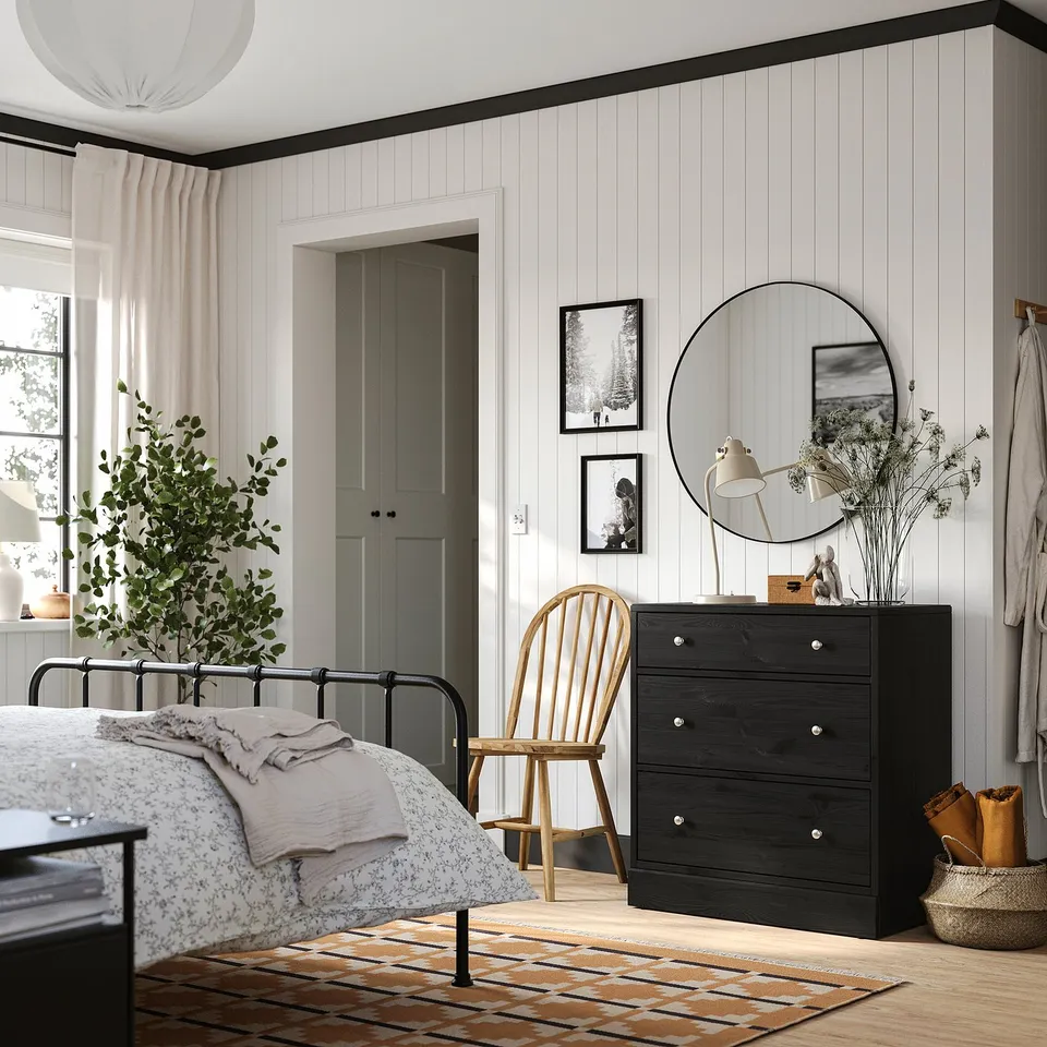 Modern bedroom with dark HAVSTA dresser, mirror, chair, and window with beige curtains.