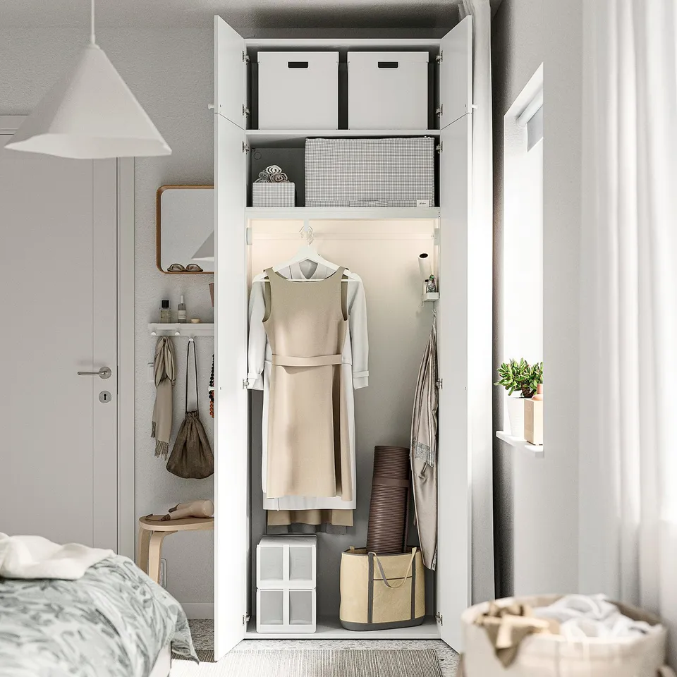 Open wardrobe with hanging dresses, folded clothes, boxes, and bags; part of a bedroom setup.