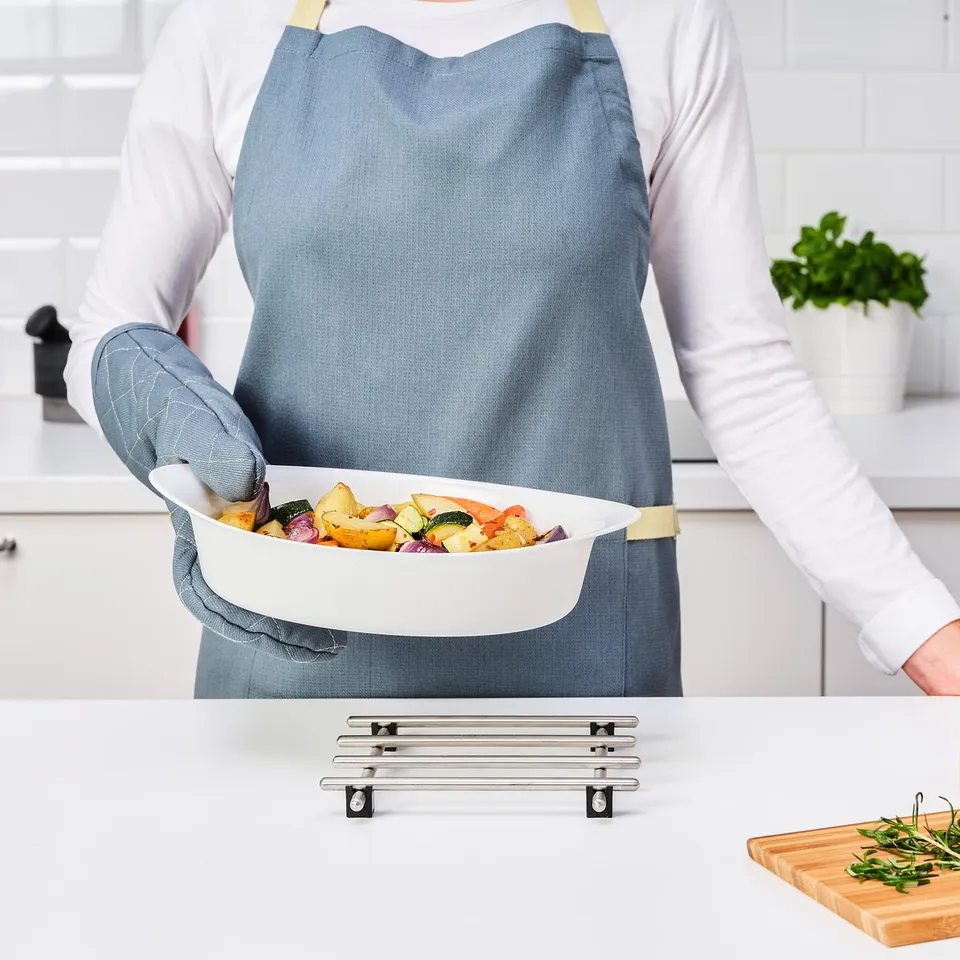 Person in apron serving roasted vegetables in LÄTTVIKTIG glass baking/serving dish, showcasing easy handling and oven-to-table functionality.