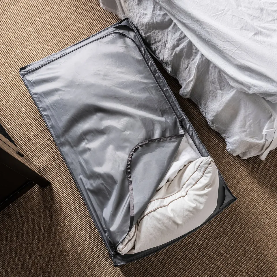An open grey SKUBB storage case on a patterned carpet, partially filled with bedding.