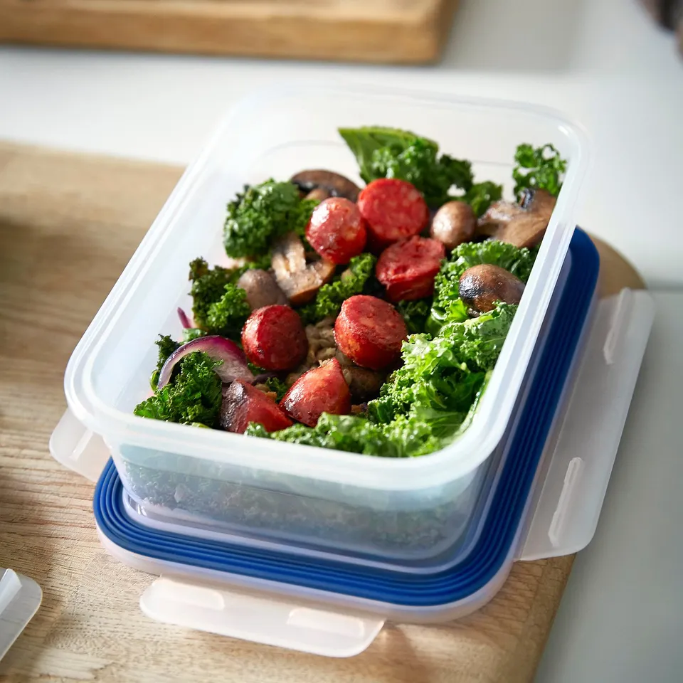Clear plastic container, blue lid, holds cooked veggies and sausage. Leak-proof, stackable, transparent.