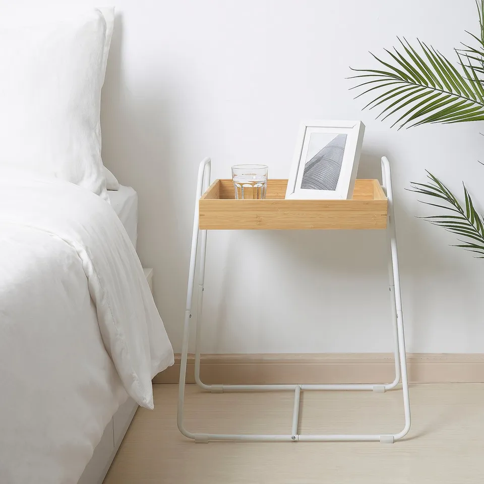 Bamboo tray side table with white metal frame, beside bed, holds glass & picture.