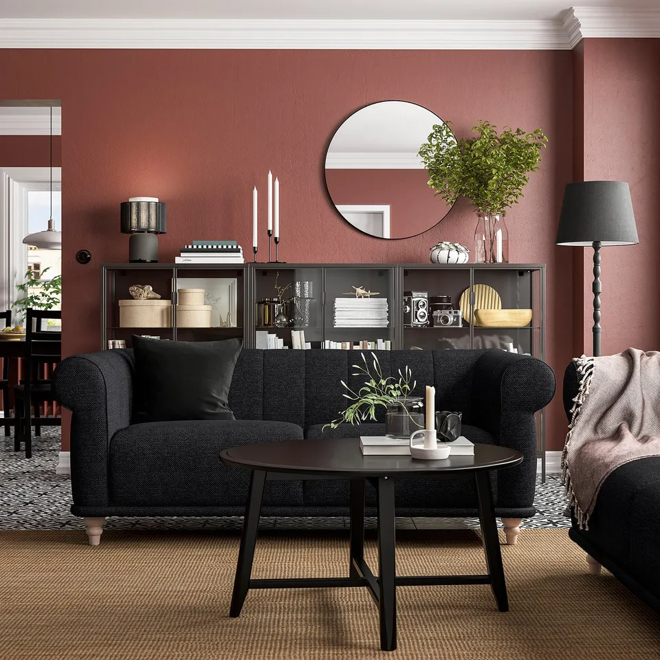 Modern living room with VISKAFORS black sofa, round coffee table, red walls, floor lamp, and decorated shelves.