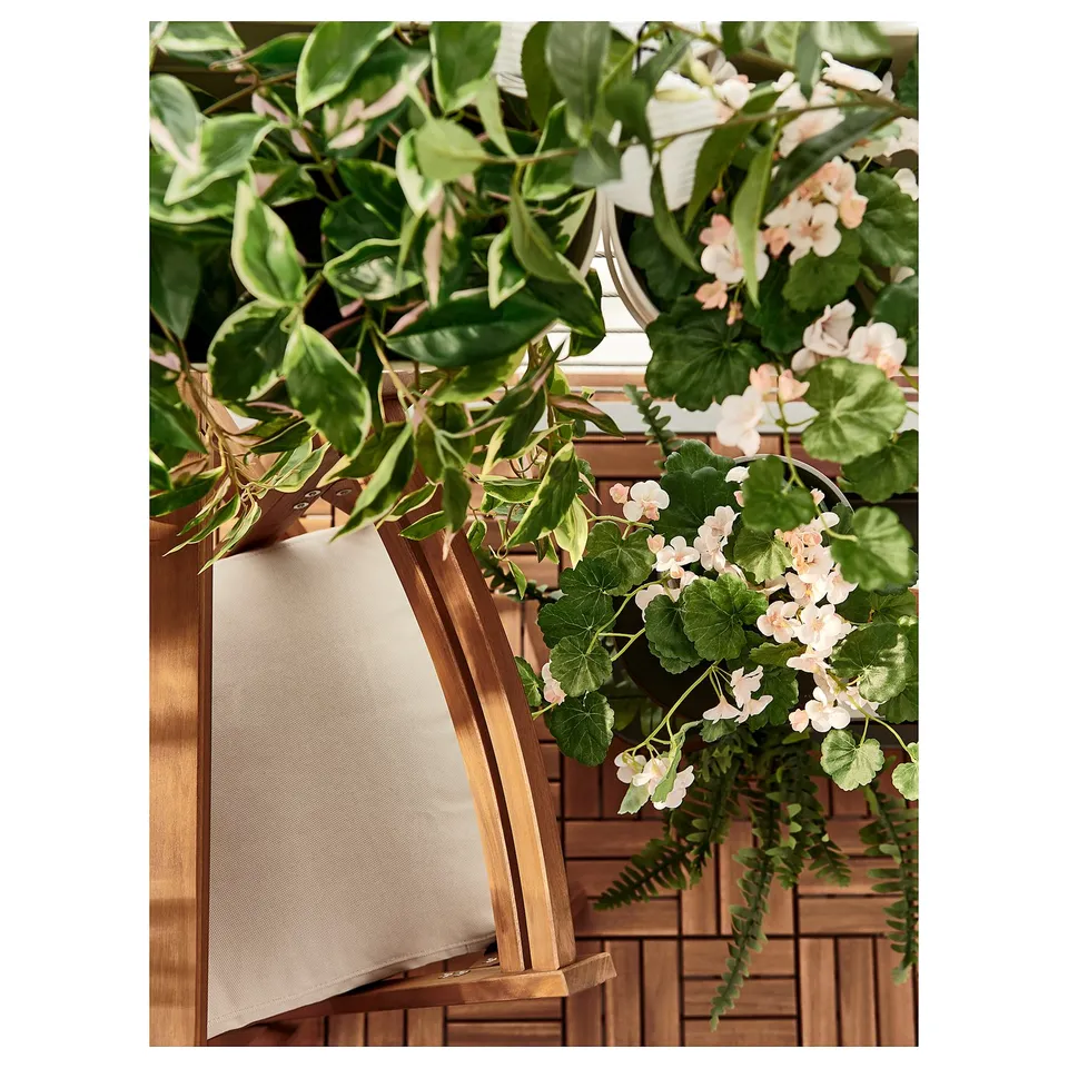 Wooden chair with white cushion, surrounded by lush green and white plants.