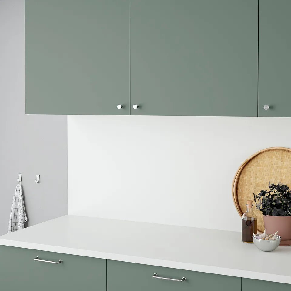 Modern kitchen counter with green cabinets and white countertop. Decorative items include a woven tray, plant, and dish.