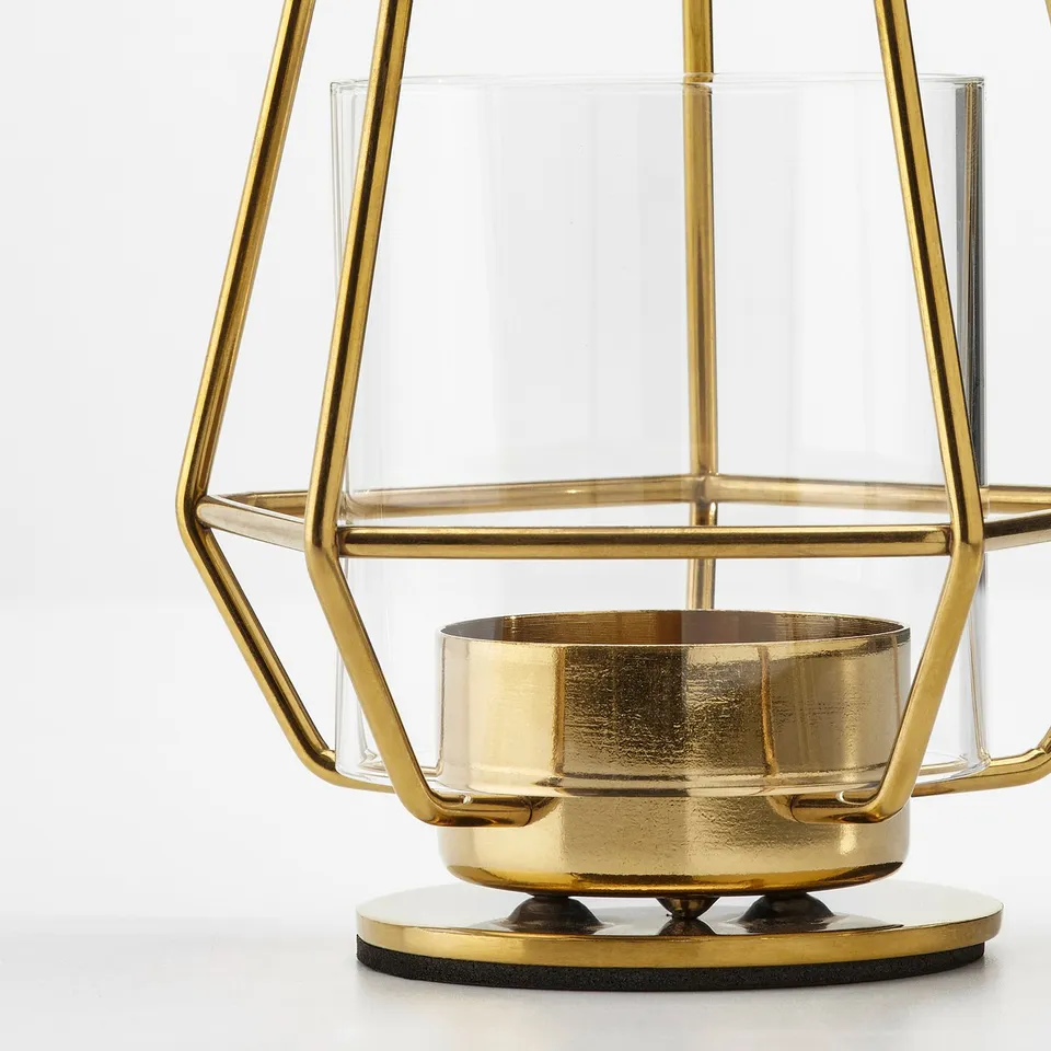 Gold-toned metal frame candle holder with clear glass panels, standing on a round base, reflecting sophisticated design and quality craftsmanship.