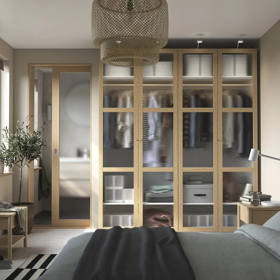 Modern bedroom with large wooden wardrobe, glass doors, and a black bed. Decorative light fixture and greenery.