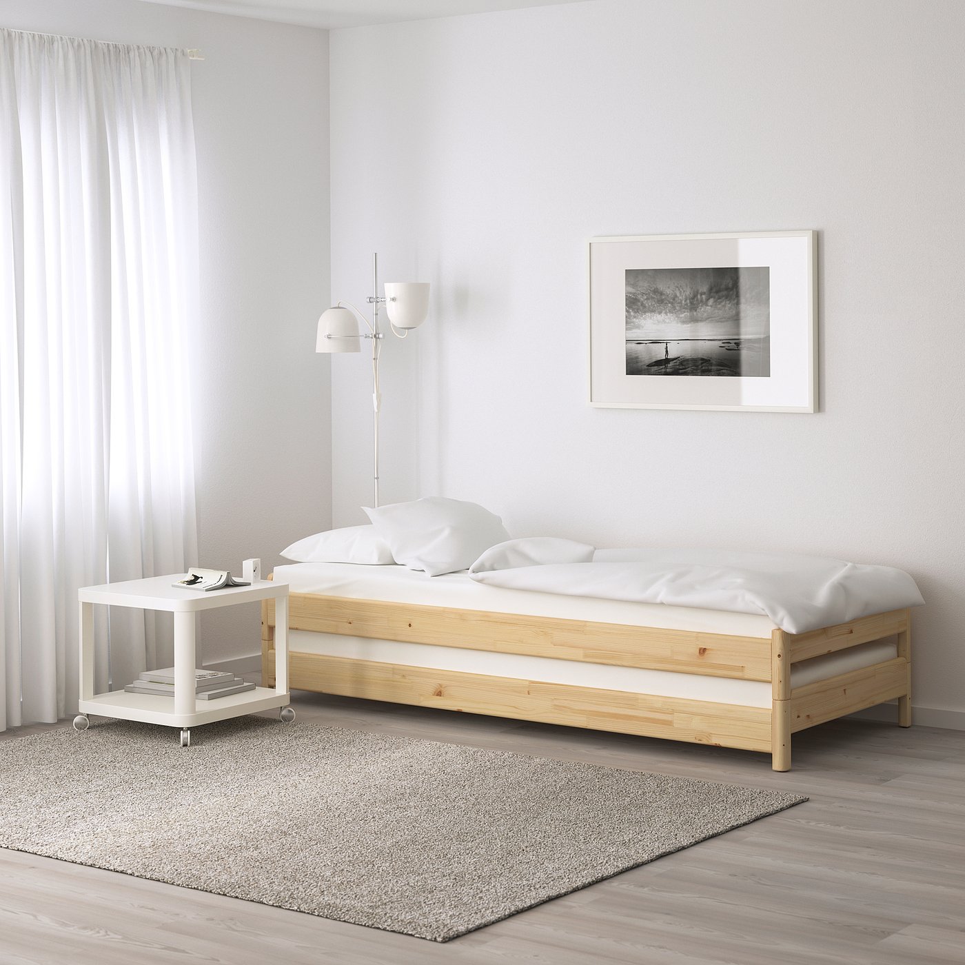 Minimalist white bedroom with wooden bed, small white side table, grey rug, and black-and-white art. Mattress is 12 cm thick.
