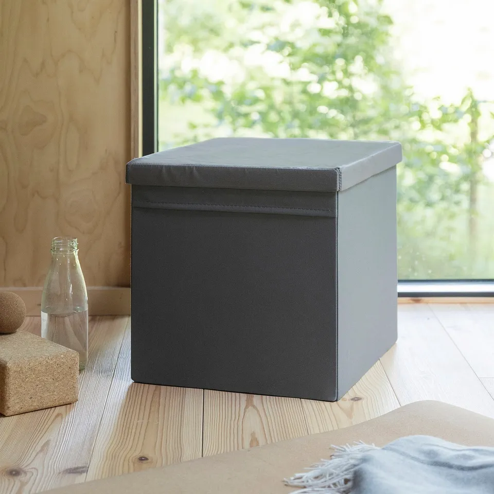 Grey fabric-covered storage box, square, fits DRÖNA, recycled polyester, sits by window, near water bottle.