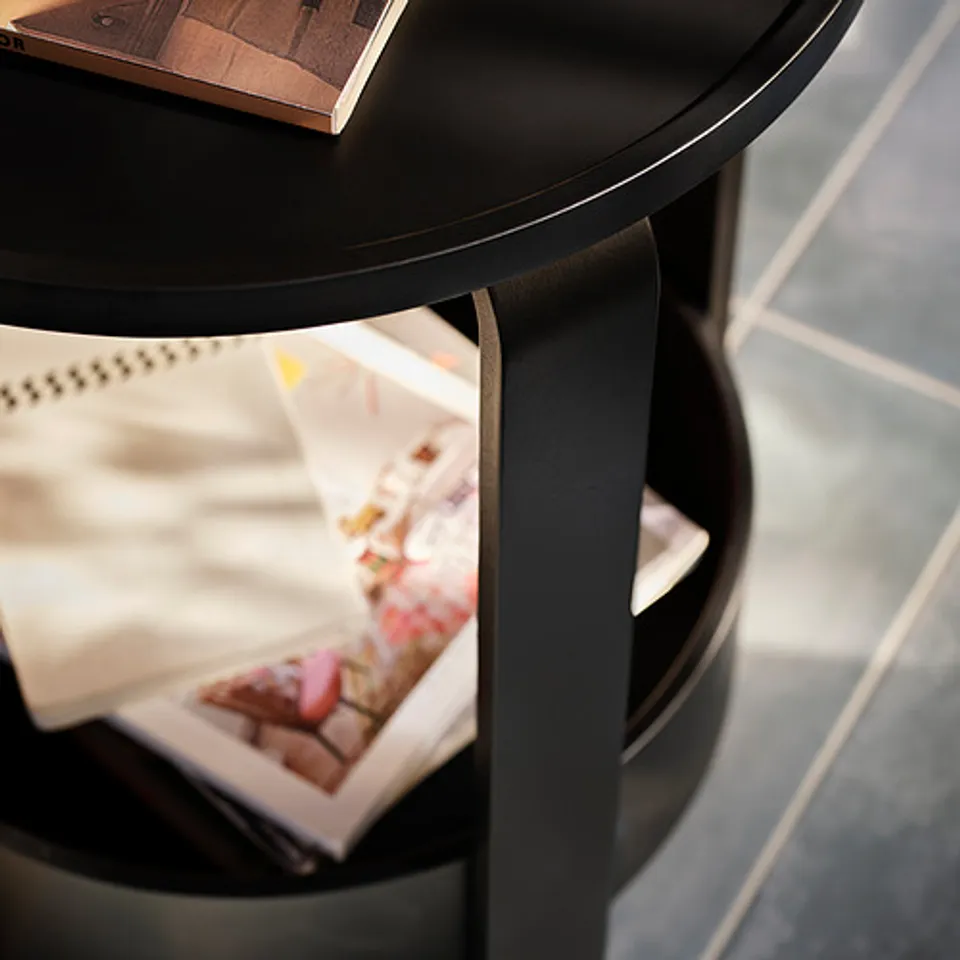 Black, round side table with smooth edge. Magazines and papers stored underneath. Elegant and functional.
