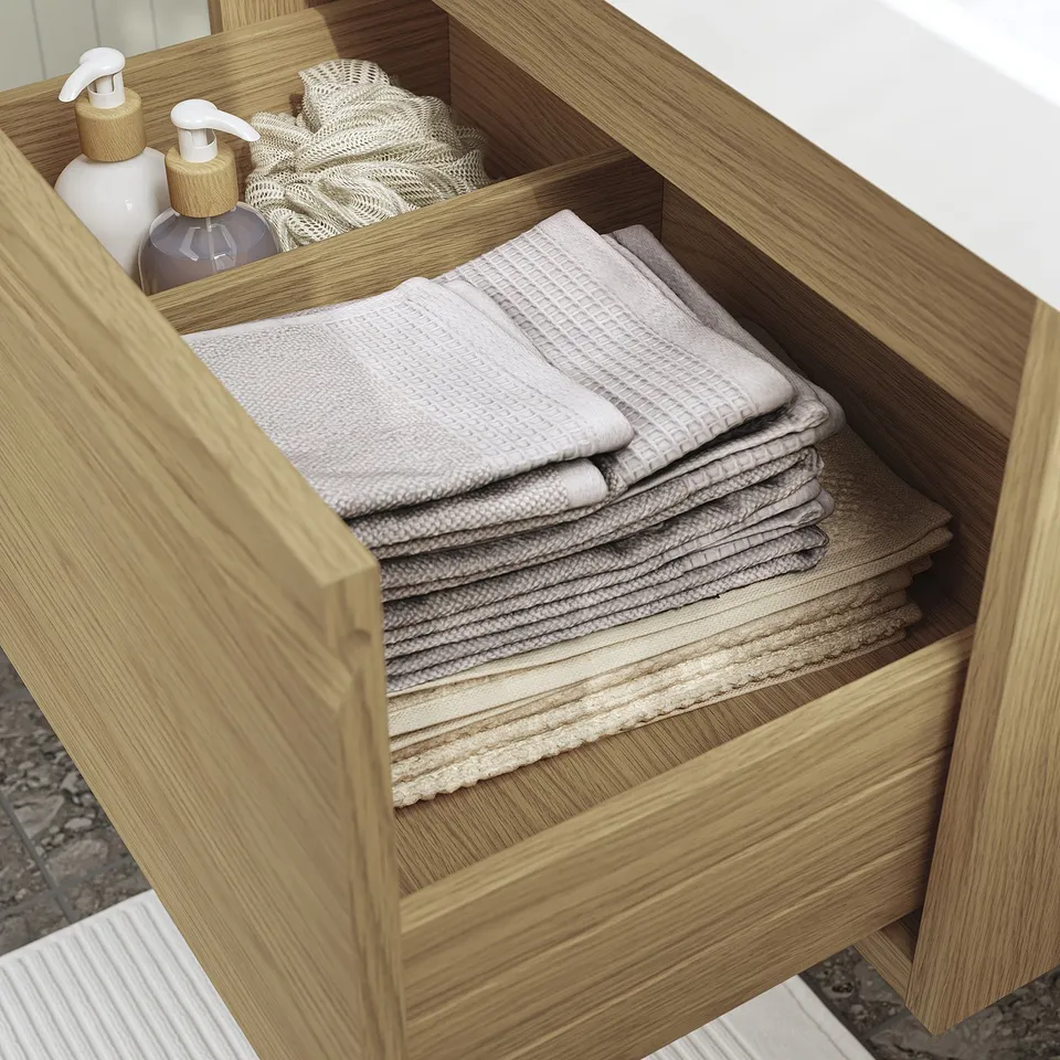 Wooden bathroom drawer with towels and liquid bottles, organised neatly.