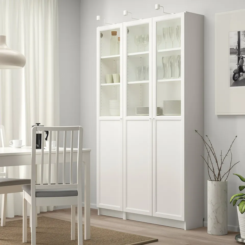 White BILLY bookcase with plates and vases, taller than chair, in modern dining room.