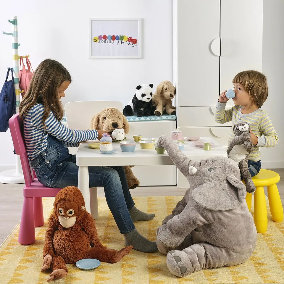 Kids seated at table with tea set, toys, and stuffed animals.