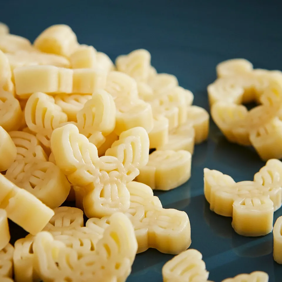 Pile of yellow pasta shaped like moose heads and flowers on a blue surface.