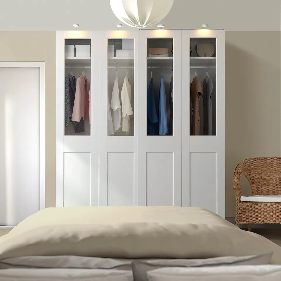 White PAX wardrobe with glass/solid doors, clothes, beside bed.