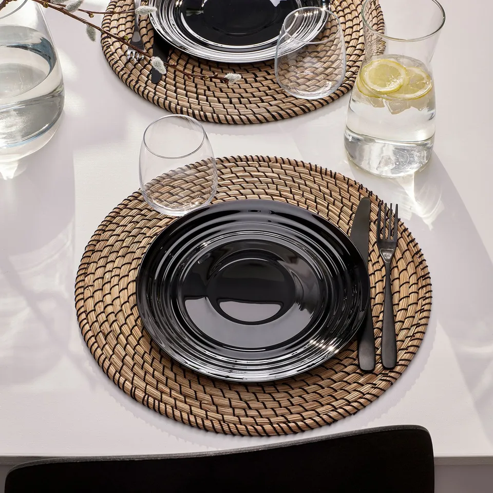 Table setting with NÄTBARB glass plates, cutlery, and woven placemats. Water glasses with lemon slices.