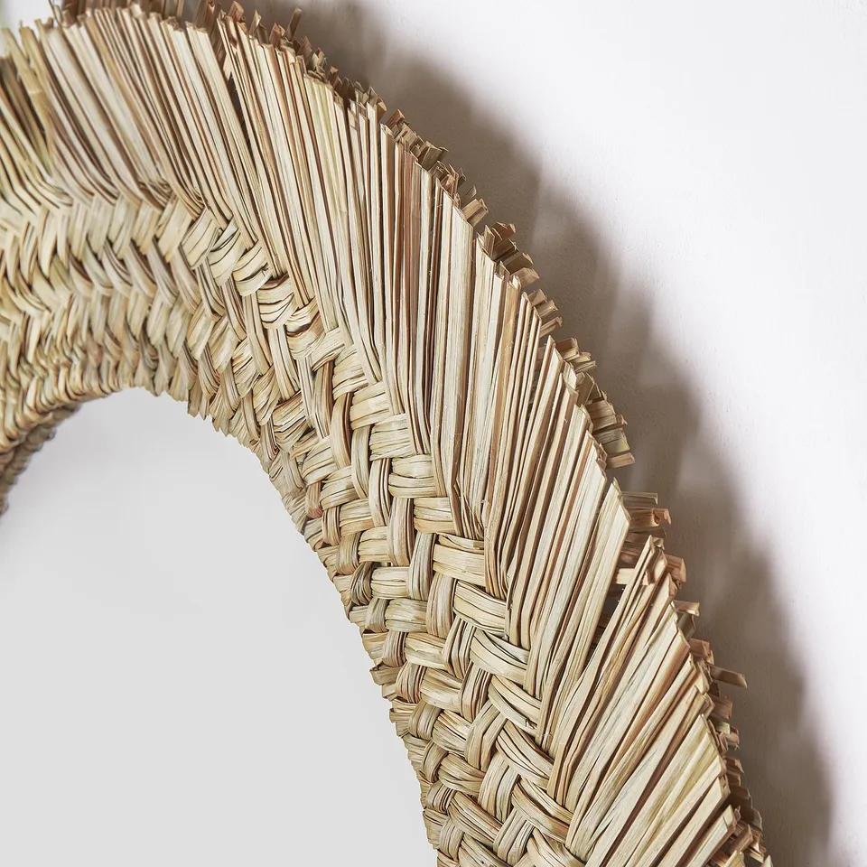 Handwoven mirror, intricate natural fibres, circular design. Light reflects off finely crafted sedge.