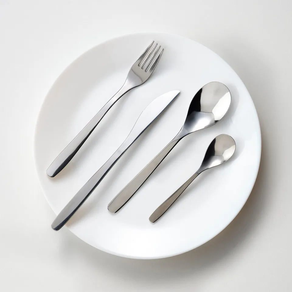 MOPSIG cutlery set: shiny steel fork, knife, spoon, and teaspoon on a white plate, modern minimalist design, durable and easy to clean.