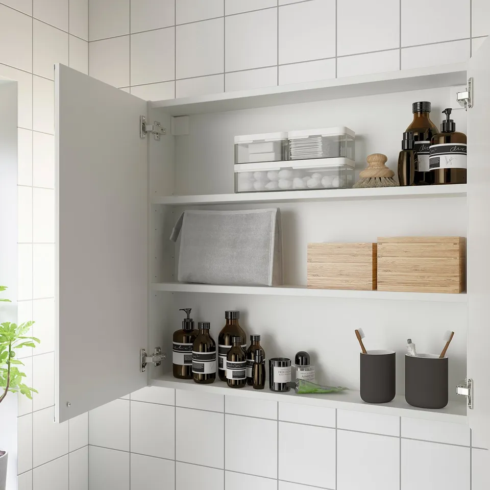 Open bathroom cabinet with mirror doors displaying shelves, holding various items like toiletries, containers, and wooden boxes.