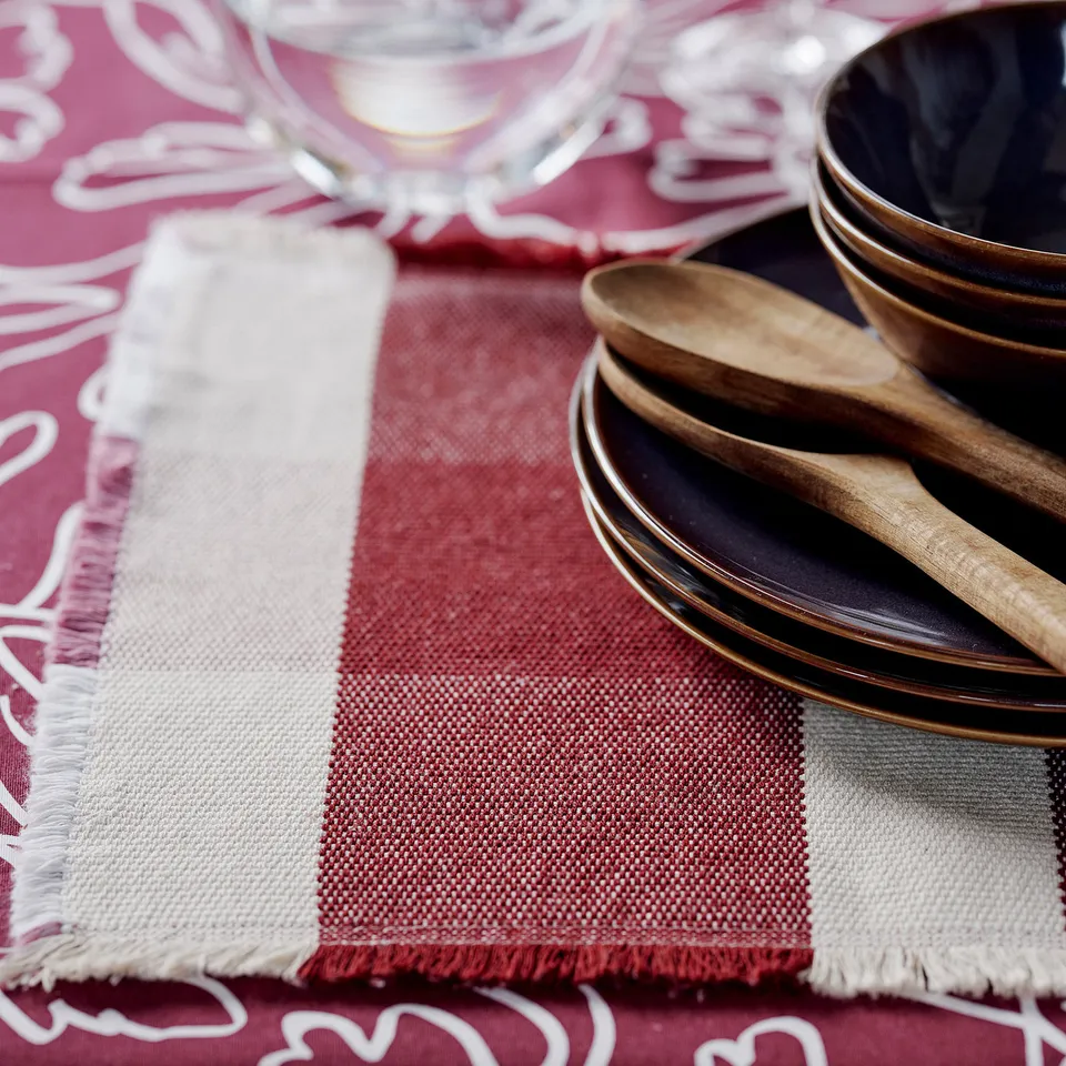 Elegant autumn table setting with woven cotton place mats, dark plates, wooden spoons, and clear glassware, exuding warmth and sophistication.