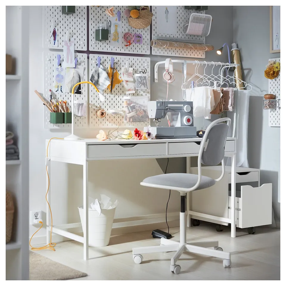 An ALEX white desk with drawers and a matching chair. It has pegboards with accessories and a sewing machine on the desk.