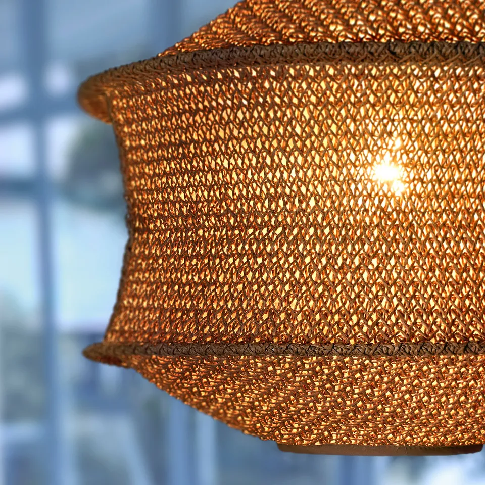 Close-up of woven hanging lamp, warm light glowing through intricate paper pattern, casting soft shadows.