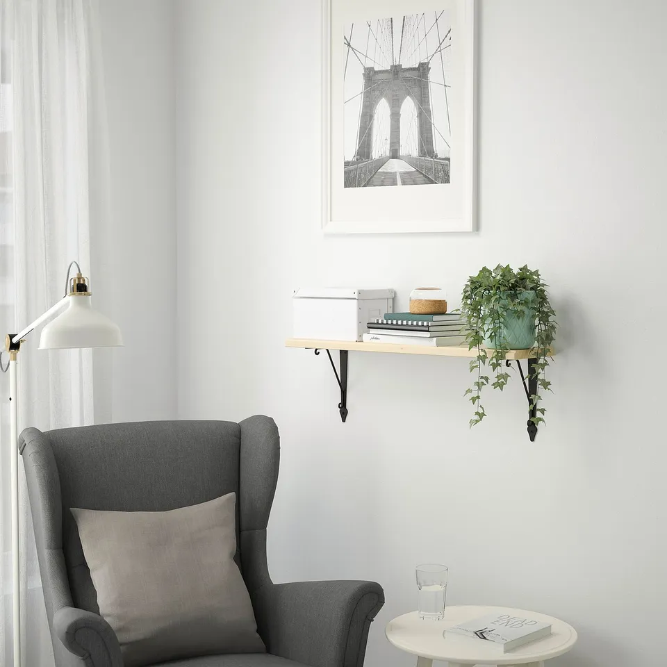 Minimalist corner with grey armchair, TRANHULT shelf, books, plant, and bridge sketch.