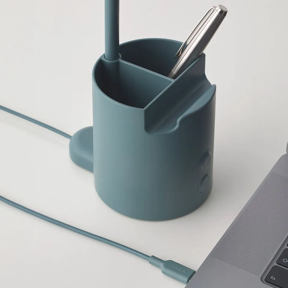 A green lamp with integrated pen holder and usb charging cable sitting on a white desk.