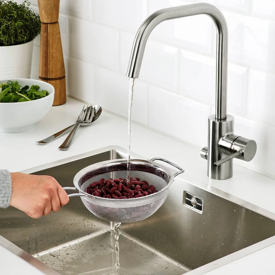 Person washing beans in a colander under a modern, stainless steel kitchen tap.