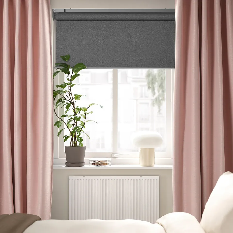 Modern bedroom with VILBORG blind, pink curtains, plant, lamp, and bed.