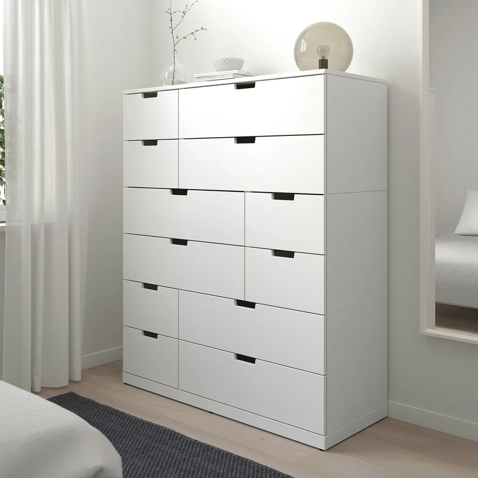 Modern white NORDLI 6-drawer chest in bedroom, tall between curtains and bed.