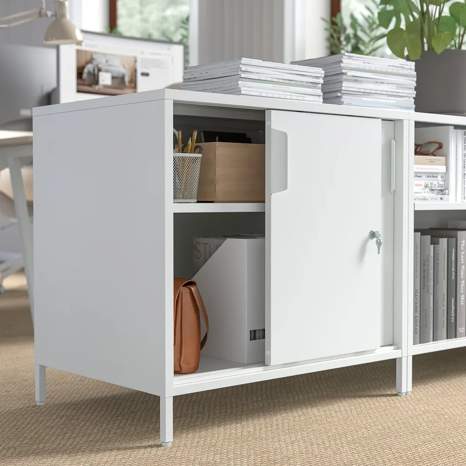 White TROTTEN cabinet with sliding doors open, showing organised storage of bags, boxes, and files.