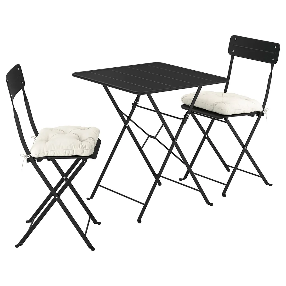 A black SUNDSÖ outdoor set with a foldable table and two chairs, each with cream-colored cushions.