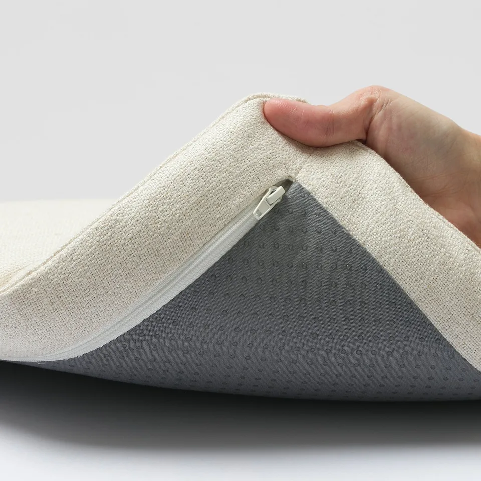 Hand holding pillow showing zip and removable cover.