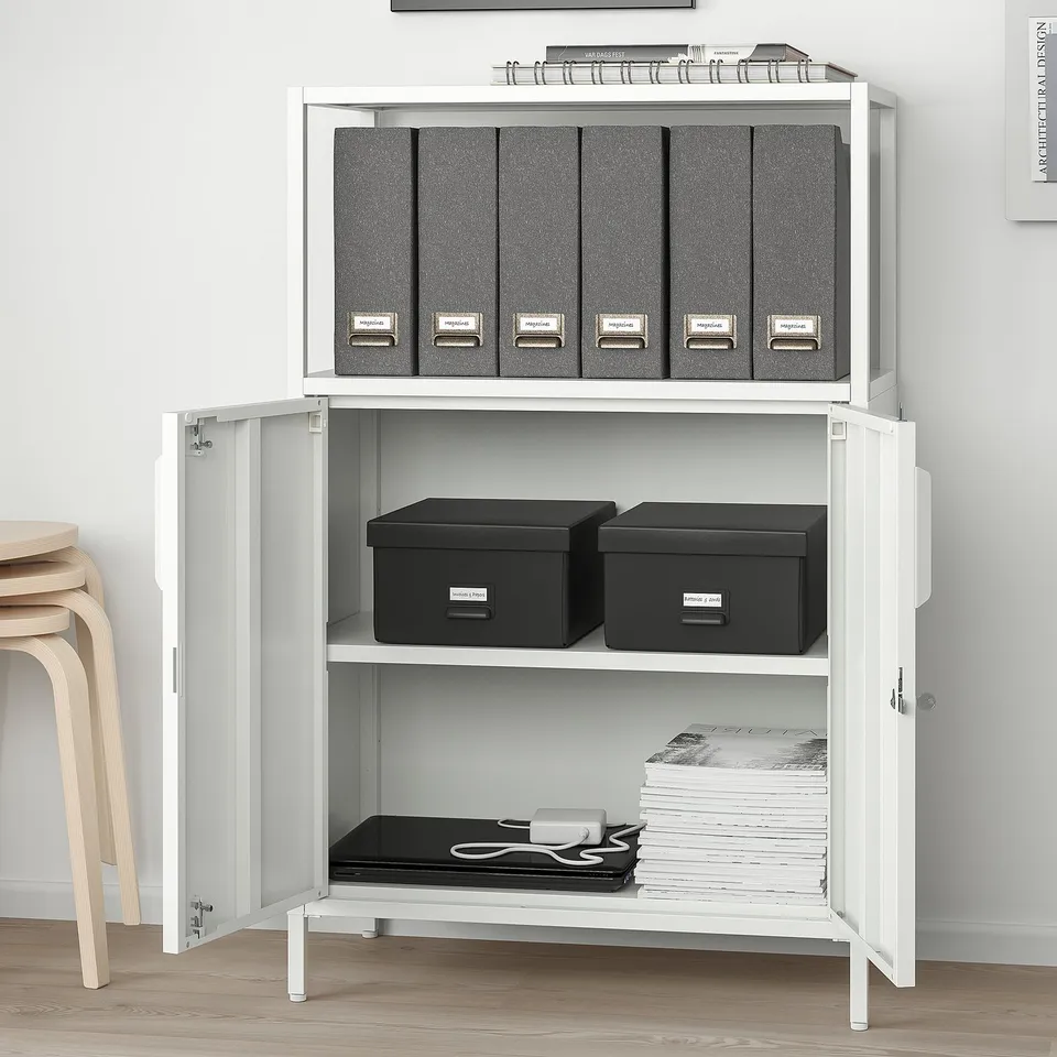 White cabinet with files, boxes, and papers. Lockable, wall-mounted.