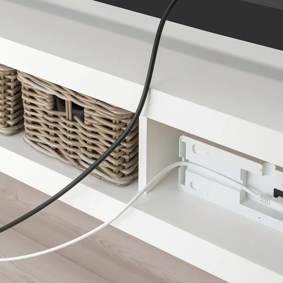 Image shows a LACK tv bench with woven baskets and visible cables. The opening at the back allows for organised wire management.