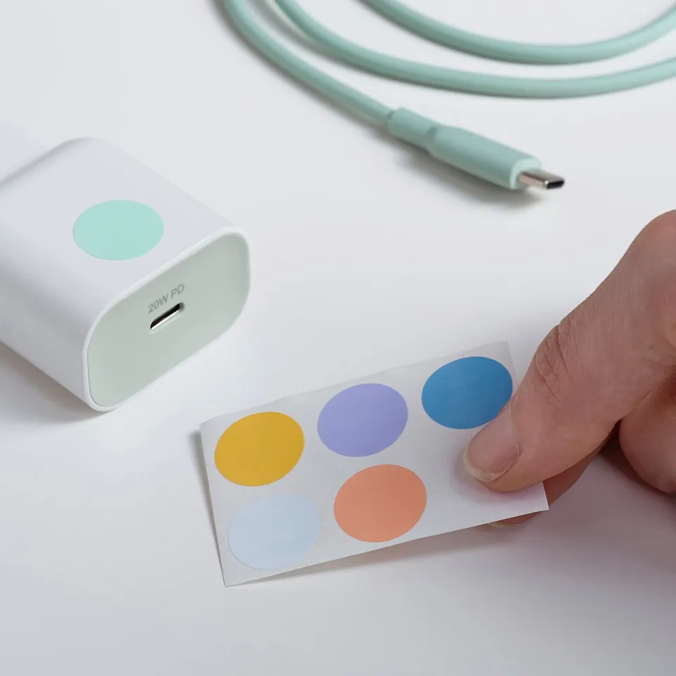 A hand peels colourful stickers near a white 20w usb-c charger with a teal cable.