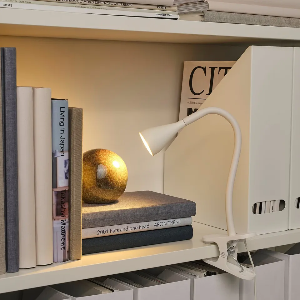 Bookshelf with white desk lamp clamped on, lighting a golden sphere on top of books.
