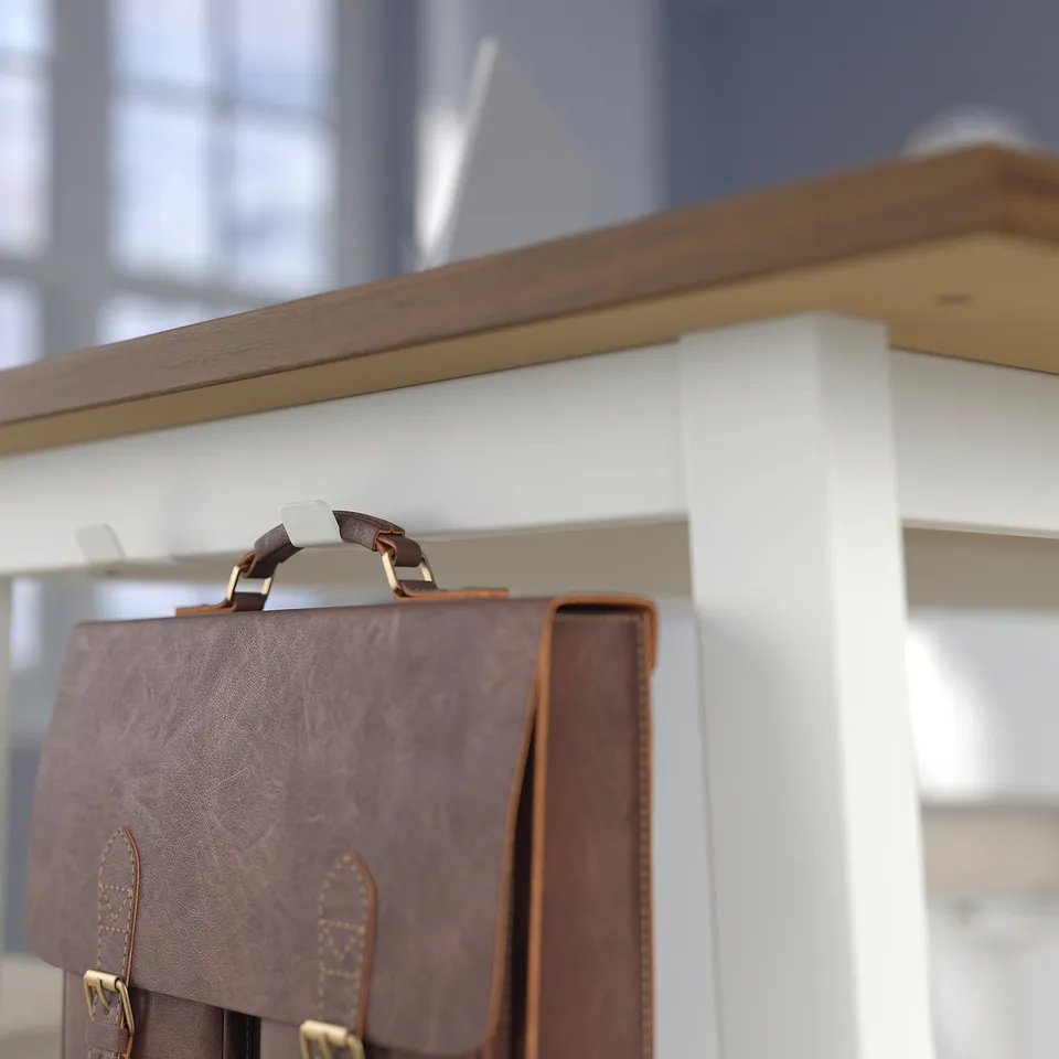 Brown leather bag hangs from a gold hook on a high, white conference table, designed for sitting or standing with footrests.