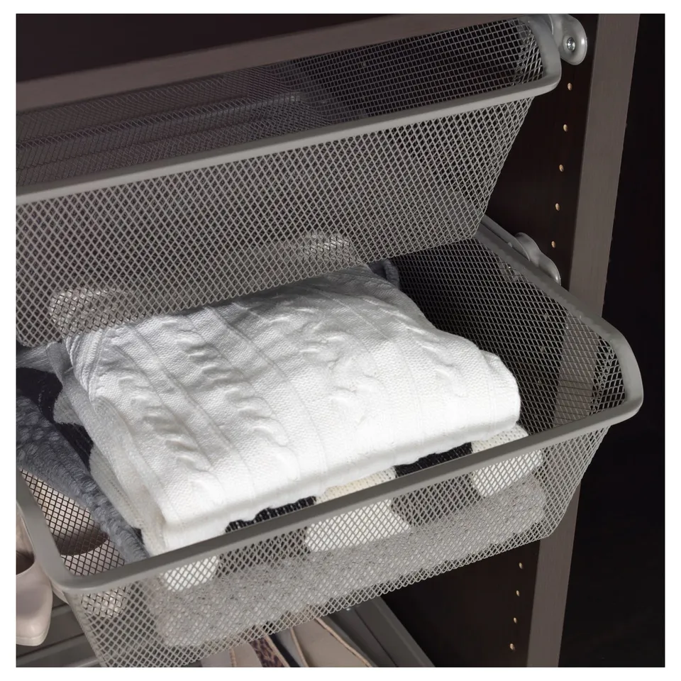 Metal mesh laundry basket with folded white clothes, part of IKEAs KOMPLEMENT series, providing ventilation and easy visibility.